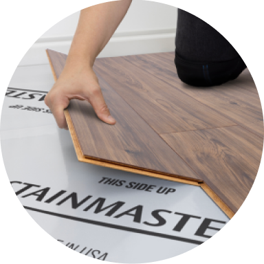 A person installing laminate flooring over Stainmaster underlayment.